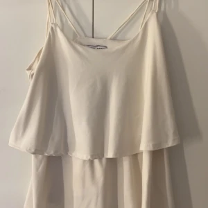 Vit topp från Vero Moda - Supersöt vit topp från Vero Moda med tunna axelband och volang upptill. Perfekt för varma dagar, enkel och stilren design som passar till sneakers eller sandaler. Lätt och luftig känsla.