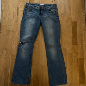 Lågmidjade bootcut jeans  - Lågmidjade bootcut jeans med ett hål över ena knät. 