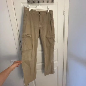 Beiga cargopants med fickor - Snygga beiga cargopants med stora sidofickor och raka ben. Byxorna har normal midja och är tillverkade i bomull, vilket gör dem både bekväma och lätta att bära. Perfekta för en avslappnad och trendig stil.