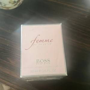 Hugo Boss Femme EdP 50ml - Hugo Boss Femme Eau de Parfum 50 ml i en elegant ljusrosa kartong. Parfymen är en naturlig spray och kommer i originalförpackning. Feminint och stilrent intryck, perfekt för dig som gillar klassiska dofter med modern twist.