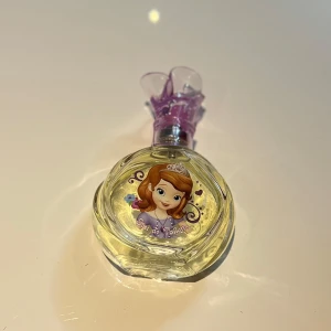 Disney Sofia the First Eau de Toilette - Söt parfymflaska med motiv av prinsessan Sofia från Disney. Rund, genomskinlig glasflaska med lila dekorlock och rosa spraydel. Perfekt för dig som gillar sagotema och vill ha en gullig detalj på sminkbordet. 50 ml, använts ett par få gånger ungefär 3 gånger.