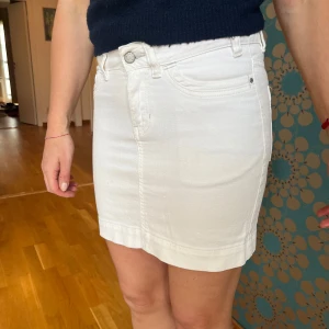 Vintage Vit jeanskjol  - Snygg vit jeanskjol med klassisk femficksdesign, bälteshällor och knappgylf. Kjolen är medellång och har raka linjer, perfekt till sneakers eller boots. Materialet är authentic denim som ger en cool och fräsch vibe.