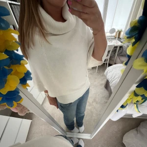 Vit stickad polotröja med vida ärmar - Säljer en vit stickad polotröja med bred polokrage och vida trekvartsärmar. Tröjan har ribbade detaljer vid krage, ärmslut och nederkant. Perfekt för en stilren och mysig look.