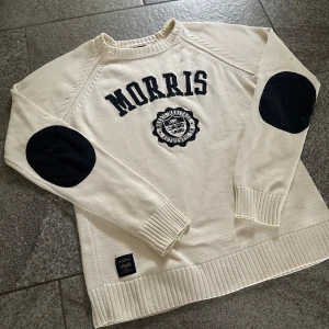 Vit stickad tröja från Morris - Säljer en vit stickad tröja från Morris med svarta detaljer och broderad logga på bröstet. Tröjan har svarta armbågslappar, ribbade muddar och rund hals. Perfekt för en stilren och klassisk look. Storlek S men skulle säga att den passar XS bättre.