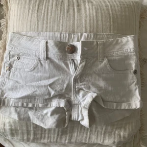 Vita lågmidjade jeansshorts - Säljer ett par vita lågmidjade jeansshorts med en stor knapp framtill. Shortsen är köpta secondhand, skriv gärna vid frågor🤍