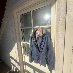 Blå vindjacka från Moncler - Säljer en blå vindjacka från Moncler med grå huva och dragkedja framtill. Jackan har Moncler-logga på ärmen och röda detaljer längs dragkedjan. Perfekt för blåsiga dagar och enkel att matcha med olika outfits. priset är inte hugget i sten!😊