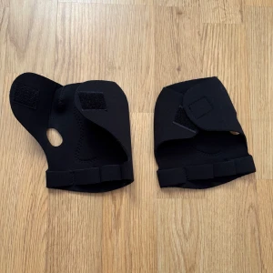 Svarta träningshandskar med kardborre - Svarta träningshandskar med öppning för tummen och justerbara kardborreband. Handskarna har förstärkt grepp på handflatan och är designade för att ge stöd vid träning. Säljs i par.