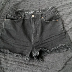 Svarta jeansshorts med fransar - Svarta jeansshorts från Bikbok. Modellen är midwaist och har knapp- och dragkedjestängning framtill. Perfekta för varma dagar och enkel att matcha med olika toppar.