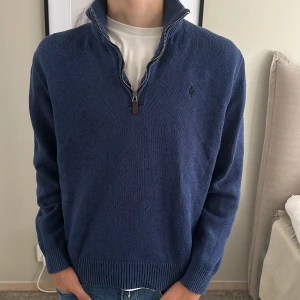Marinblå stickad tröja från Ralph Lauren - Säljer en marinblå stickad tröja från Ralph Lauren med half zip och hög krage. Tröjan har diskret broderad logga på bröstet och ribbade muddar vid ärmslut och nederkant. Perfekt för lager-på-lager och chill stil.