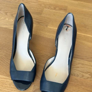 Svarta pumps med öppen tå från Nine West - Säljer ett par klassiska svarta pumps från Nine West med öppen tå och smal klack. Skorna är i skinn och har en elegant, tidlös design som passar till många olika outfits.
