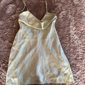 Ljusgrön kortklänning från NA-KD - Säljer en ljusgrön kortklänning från NA-KD med tunna axelband och snygg draperad urringning. Klänningen är i stan och är perfekt för varma dagar. Enkel och stilren design som passar till många tillfällen.