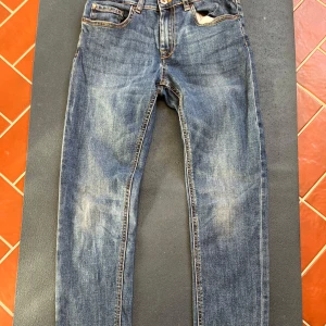 Blå slim stretch jeans från Converse - Säljer ett par blå slim stretch jeans från Converse med klassiska fem fickor och snygga kontrastsömmar. Jeansen har knapp och dragkedja framtill samt läderpatch med logga bak. Perfekta för en avslappnad stil.