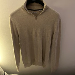 Beige tröja från Jack & Jones  - Säljer en stilren beige half-zip från Jack & Jones. Passar bra till både jeans och chinos med en skjorta eller T-shirt under. Ett litet hål som man ser på bilden där av priset.
