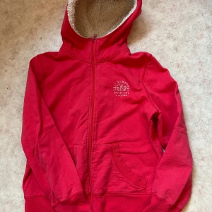 Röd hoodie från Ellos - Säljer en mysig röd kofta från Ellos med dragkedja och fodrad med mjuk fleece. Perfekt för kyliga dagar med sin varma huva och praktiska fickor framtill. Märket JSFN syns på etiketten. Storlek 38 ♥️
