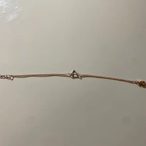 Guldarmband med triangeldetalj - Elegant guldarmband med en minimalistisk triangeldetalj i mitten. Armbandet har en tunn kedja och justerbar längd med klolås. Perfekt för att lägga till en subtil touch av stil till din outfit.