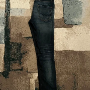 Mörkblå jeans från Jack & Jones - Snygga mörkblå jeans från Jack & Jones med slim/straight passform. Klassisk design med fem fickor och kontrastsömmar. Perfekta för en stilren look. 28/32