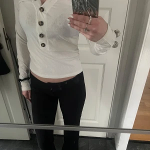 Vit ribbad tröja från Bik Bok - Säljer en stilren vit ribbad tröja från Bik Bok med knappar framtill. Tröjan har en v-ringad design och långa ärmar, perfekt för en avslappnad look. Passar bra till både jeans och kjol.