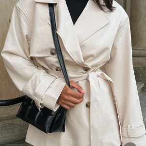 Beige trenchcoat med bälte - Snygg beige trenchcoat med knappar och bälte i midjan. Jackan har långa ärmar och en klassisk krage. Perfekt för vår och höst. Säljer pågrund av att den var förstor för mig. Prislappen sitter kvar. Storlek 34 men känns som en 36. Kostade 1000kr hos NAKD.