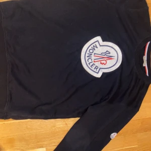 Svart tröja från Moncler - Snygg svart tröja från Moncler med ett stort, broderat logotypmärke på framsidan. Tröjan har långa ärmar och en rund halsringning. Perfekt för en stilren och avslappnad look.