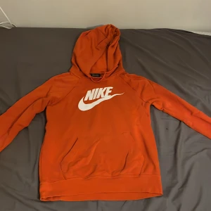 Orange hoodie från Nike - Säljer en snygg orange hoodie från Nike med klassisk logga i vitt på bröstet. Tröjan har en bekväm passform med långa ärmar och en praktisk huva. Perfekt för en avslappnad stil.