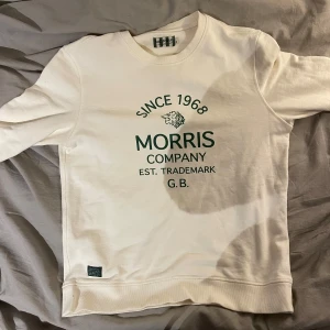 Vit sweatshirt från Morris - Säljer en stilren vit sweatshirt från Morris med tryck framtill. Tröjan har rund hals och långa ärmar, perfekt för en avslappnad stil. Märket är känt för sin kvalitet och tidlösa design.