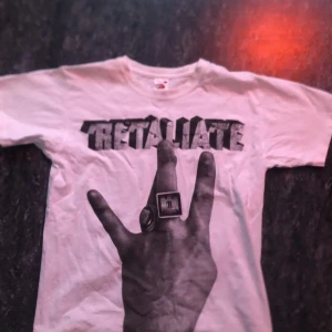 Vit t-shirt med tryck Retaliate - Cool vit t-shirt med tryck av en hand och texten 'RETALIATE' i svart. Perfekt för en avslappnad stil. Tillverkad i bomull för en skön känsla.