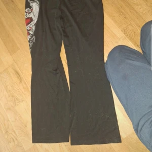 Svarta byxor med drakmotiv - Snygga svarta byxor med ett coolt drakmotiv på sidan. Byxorna har en rak passform och är perfekta för en unik stil. De är tillverkade i ett mjukt material som ger en bekväm känsla hela dagen.