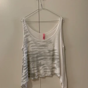 Vit och gråmönstrad linnetopp från Retro doll - Säljer en vit och gråmönstrad linnetopp. Toppen har en lös passform och är ärmlös med ett avslappnat snitt. Perfekt för varma dagar eller som ett lager under en jacka.