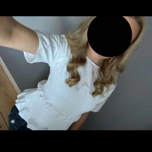 Vit ribbad blus - Säljer en söt vit blus med ribbad struktur och volangdetaljer i midjan. Blusen har korta ärmar och en smickrande passform. Perfekt för en stilren look!