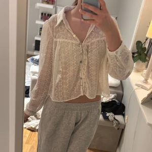 Vit blus med spetsdetaljer - Säljer en söt vit blus med spetsdetaljer och knappar framtill. Den är inte stor för vara M. Blusen har långa ärmar och en luftig passform, perfekt för vår och sommar. Den har en fin krage och ett delikat mönster.