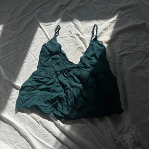 Mörkgrön linnetopp - Säljer en mörkgrön linnetopp med smala axelband och v-ringning. Toppen har en lös passform och är perfekt för varma dagar. Materialet är lätt och luftigt, vilket gör den bekväm att bära.