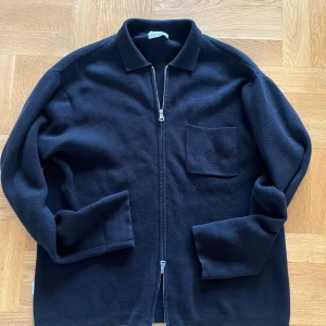 Svart Vårjacka från Studio Total - Snygg svart jacka från Studio Total med dragkedja och en bröstficka. Jackan har en klassisk krage och långa ärmar, perfekt för en stilren look. Passar bra till både vardag och mer uppklädda tillfällen.