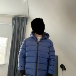 Blå dunjacka från Rossignol - Säljer en snygg blå dunjacka från Rossignol. Jackan har en dragkedja framtill och är långärmad med ribbade muddar. Perfekt för kyliga dagar med sitt varma och bekväma material. Inuti finns ett coolt bergsmotiv som ger en extra touch.