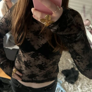 Svart spets topp - Säljer en snygg svart spets topp med långärmad design. Toppen är genomskinlig och har ett blommigt mönster som ger en elegant touch. Perfekt för att lägga till en extra dimension till din outfit.