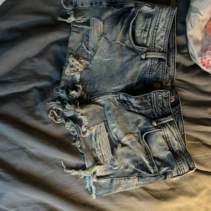 Blå jeansshorts från Bershka - Säljer ett par snygga blå jeansshorts från Bershka med fransiga kanter och slitna detaljer. Perfekta för en avslappnad sommarlook. De har klassisk femficksdesign och knappgylf. Passar perfekt för varma dagar!