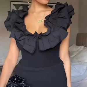 Svart body från Zara - Säljer en elegant svart body från Zara med volangdetaljer runt halsen. Toppen är ärmlös och har en tight passform, perfekt för en stilren look. Populär och slutsåld. Passar xs-m