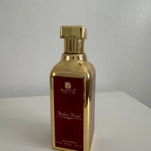 Ambre Rouge Eau de Parfum från Riiffs - Elegant flaska i guld med röd etikett, Ambre Rouge från Riiffs. Innehåller 100 ml Eau de Parfum med en lyxig och förförisk doft. Perfekt för den som vill ha en sofistikerad och unik doftupplevelse.