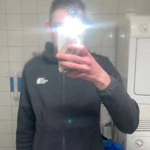 Grå fleecejacka från The North Face - Säljer en grå fleecejacka från The North Face. Jackan har en dragkedja framtill och är långärmad. Perfekt för kyliga dagar och sköna promenader. Passar bra till både vardag och äventyr.