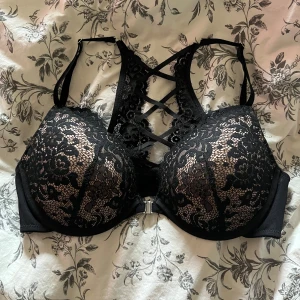 Svart spets-BH från Hunkemöller push up  - Säljer en elegant svart BH från Hunkemöller med vacker spetsdetalj och korsade band i ryggen. BH:n har vadderade kupor och en bekväm passform. Perfekt för att känna sig extra fin! 💖