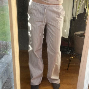 Randiga linnebyxor med låg midja - Säljer ett par bekväma linne byxor med randigt mönster och dragsko i midjan. De är i en ljus färg med tunna ränder.