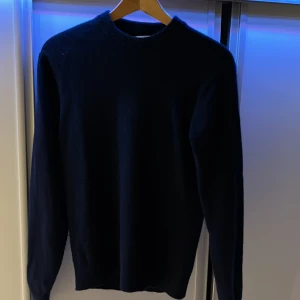 Mörkblå stickad tröja - Säljer en stilren mörkblå stickad tröja med rund hals. Perfekt för kyligare dagar och enkel att matcha med olika outfits. Tröjan har långa ärmar och en klassisk passform.