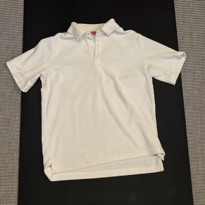 Vit kortärmad pikétröja från RYVLS - Säljer en klassisk vit kortärmad pikétröja från RYVLS. Perfekt för en stilren och avslappnad look. Tröjan har en krage och knappar framtill. Passar utmärkt till både vardag och mer uppklädda tillfällen. Som känns som en handduk