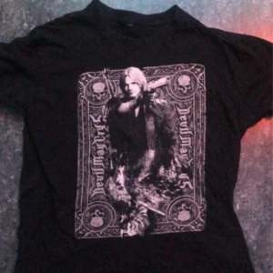 Svart t-shirt med Devil May Cry  - Säljer en svart t-shirt med ett coolt tryck från Devil May Cry. Motivet visar en karaktär med detaljerade mönster och text. Perfekt för fans av spelet! 🎮