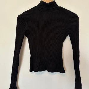 Svart polotröja från H&M - Säljer en stilren svart ribbad polotröja från H&M. Tröjan har långa ärmar och en klassisk polokrage.