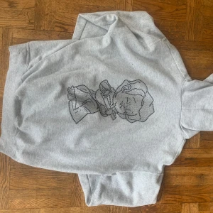 Grå hoodie med strassdetaljer från Acne Studios - Snygg grå hoodie från Acne Studios med strassdetaljer som bildar text på framsidan. Tröjan har en bekväm passform med långa ärmar och en klassisk huva. Perfekt för en stilren och avslappnad look.