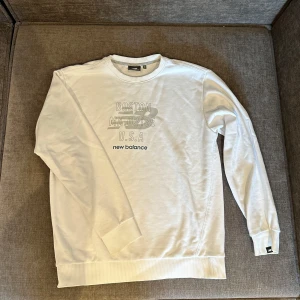 Vit sweatshirt från New Balance - Säljer en stilren vit sweatshirt från New Balance med tryck som refererar till Boston, USA. Tröjan har långa ärmar och en rund halsringning. Perfekt för en avslappnad stil. Storlek M sitter som S