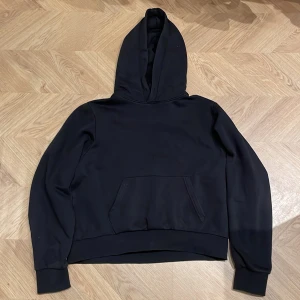 Svart hoodie från Weekday - Säljer en stilren svart hoodie från Weekday, Natalie mini hoodie. Den har en klassisk design med en stor ficka framtill och en bekväm huva. Väldigt kort i passformen, knappt använd.
