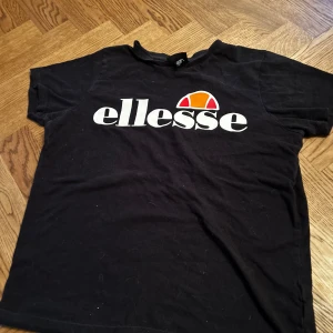 Svart t-shirt från Ellesse - Säljer en svart t-shirt från Ellesse med deras ikoniska logga i vitt och orange på bröstet. Perfekt för en avslappnad stil. Passar bra till jeans eller shorts.