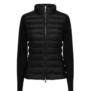  dunjacka från Moncler - Snygg svart dunjacka från Moncler med dragkedja och knappar. Jackan har långa ärmar och ett stilrent märke på ärmen. Perfekt för kyligare dagar med sin quiltade design.