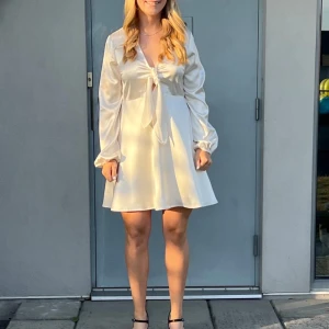 Studentklänning med knytning - Vit/champagnefärgad klänning i glansigt och luftigt material, perfekt för till exempel studenten. Den är använd endast på studentdagen.